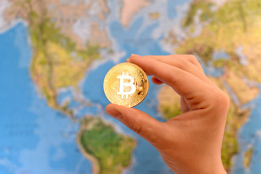 Hand holding gold coin of Bitcoin against map of world. Bitcoin concept. New world currency.
