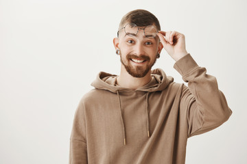 What nice surprise to see you near this copy space. Pleased handsome young european man taking off stylish glasses, smiling with satisfaction and amazement, seeing wonderful things over gray wall