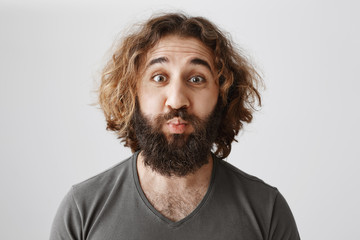 Lonely man wants romance. Studio shot of funny mature eastern male coworker with curly hair puckering, wanting to have kiss or mwah in cheek, over gray wall. Silly guy knows nothing about kisses