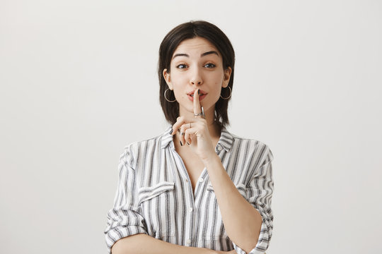 Low Your Voice, Please. Portrait Of Cute Friendly Woman In Trendy Clothes Showing Shh Gesture, Saying Shush With Index Finger Over Mouth, Being Calm And Kind While Whispering Not To Wake Up Child