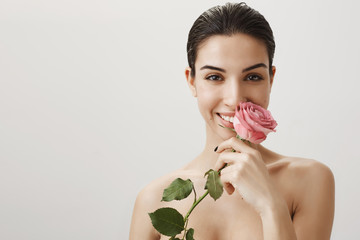 Charming woman received unexpected gift from husband. Good-looking beautiful girlfriend standing naked after showering and washing hair holding perfect rose and smelling it, smiling sensually