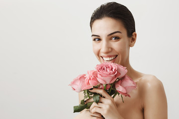 Girl is laughing from happiness after receiving bouquet of roses. Studio shot of good-looking feminine woman getting dressed while preparing to work, receiving flowers from unknown person