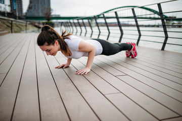 Fototapeta na wymiar Doing push-ups outdoors. Fit girl exercising at city quay.