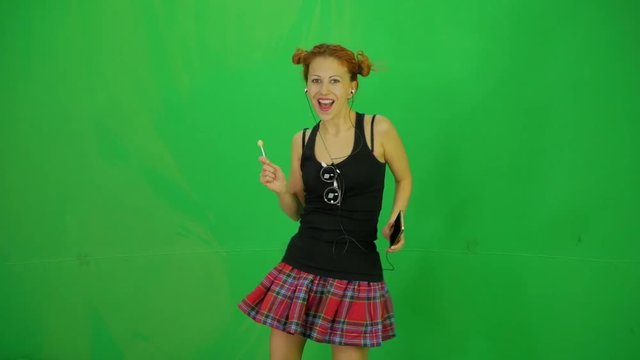 Schoolgirl with short plaid skirt and lollipop listing music by mobile phone and dancing at green-screen 50fps 