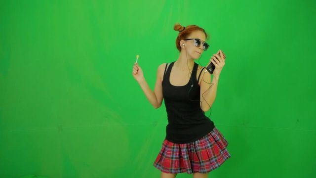 Fashion red hair young girl with lollipop and sunglass listing music by mobile and dancing at green-screen 50fps