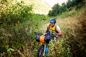 Obraz premium Biker pushes his bicycle up in high Caucasus mountains