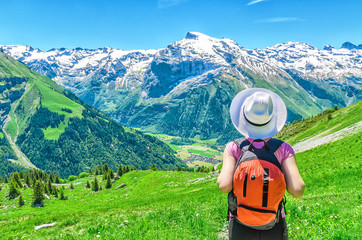 Swiss Alps. A girl in a white hat and a red backpack admiring the panoramic view of the Alpine...