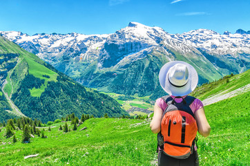 Swiss Alps. A girl in a white hat and a red backpack admiring the panoramic view of the Alpine mountains. Landscape of the Swiss Alps, the Engelberg resort.