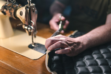 Sewing process of the leather belt. old Man's hands behind sewing. Leather workshop. textile vintage sewing industrial