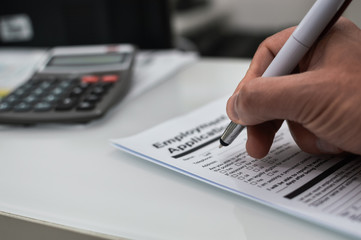 Closeup on hand of a person signing document contract form on light table background