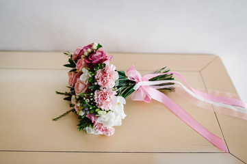 Stylish wedding bouquet bride of pink roses, white carnation and green flowers and greens with ribbons lying on pastel table. Close up. Side view. Wedding decor. Artwork.