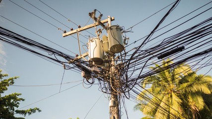 Power lines in the city. Transformers and phone lines against bright blue sky.