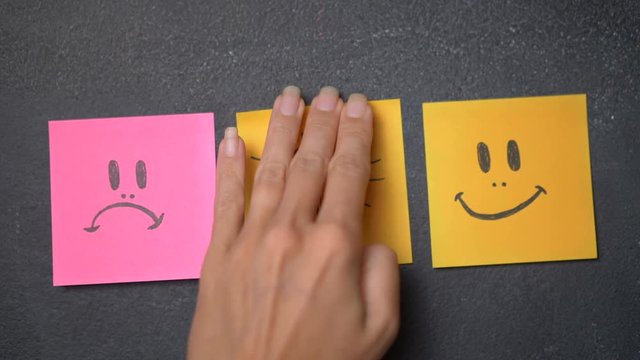 Closeup woman's hand sticking note with happy face icon on the blackboard. Change from sad to happy face - video in slow motion