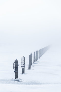 Piles stick out of a frozen lake with fog in the background. © Kilman Foto