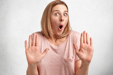 Portrait of emotional shocked young female model makes stop gesture, denies to do something,...