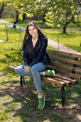 Obraz premium Glamorous young Caucasian woman in black leather jacket sitting in the park on the bench