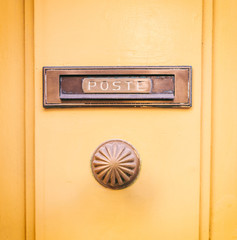 Old brass mail letter box and knob on a yellow painted front door, text poste