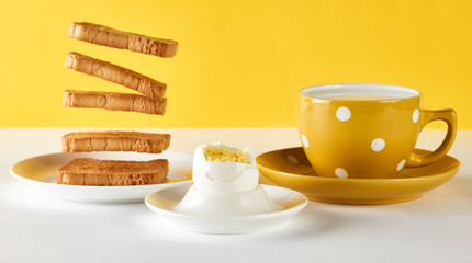 Flying toasts for breakfast and cup of fresh milk with chicken egg on white and yellow background. Levitation food and healthy vegetarian breakfast concept.