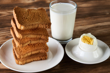Breakfast with egg, toasts and glass of fresh milk on a rustic wooden table background, close-up. Healthy vegetarian breakfast and diet concept. Levitation food concept