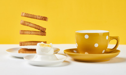 Flying toasts for breakfast and cup of fresh milk with chicken egg on white and yellow background. Levitation food and healthy vegetarian breakfast concept.
