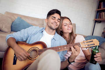 Lovely young couple playing guitar at home