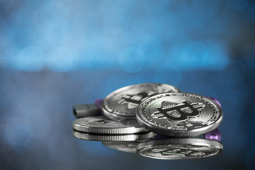 Pile of silver bitcoin cryptocurrency coins with purple digital hardware wallet on blue background with copy space.