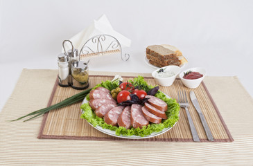 Smoked sausage with tomatoes and lettuce leaves on a plate.