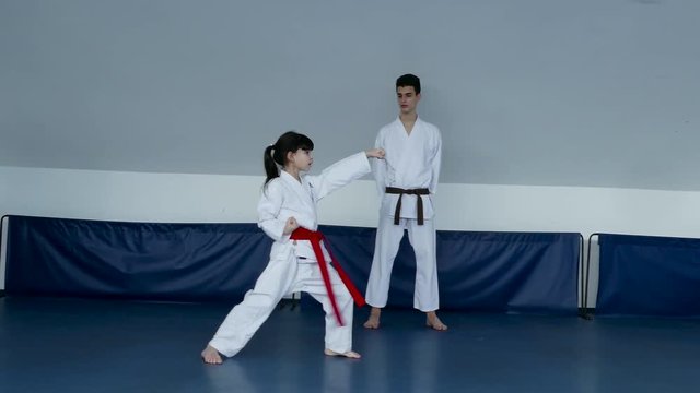 Little karate girl practicing karate moves with trainer observation.