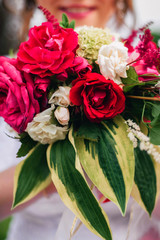 wedding bouquet with red peonies and green leaves in the hands of a happy bride with a smile