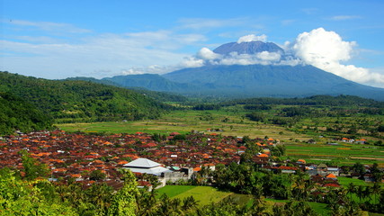 Fototapeta na wymiar malerisches Dorf zwischen grünen Reisfeldern vor Vulkan Mt.Agung in Bali bei blauen Himmel