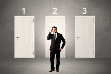 Fototapeta premium Businessman in grey room with three numbered white door behind his back 
