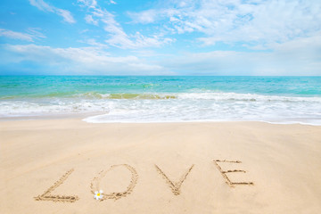 Inscription Love written on the sandy beach with ocean wave - honeymoon on beach concept.
