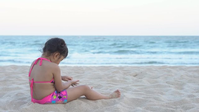 Asian children cute or kid girl sit on beach or blue sea and playing white sand alone for travel on summer holiday relax with happy fun and wear bikini with space on 4K