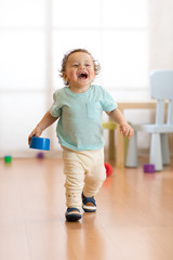 First steps of baby toddler learning to walk in living room. Footwear for little kids.