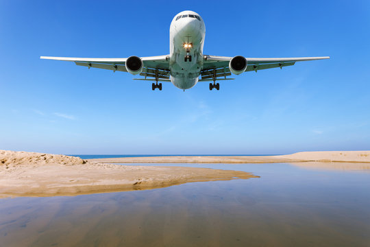 Airplane landing above Beautiful tropical sea with white sand on the beach and clear blue sky at phuket thailand image for summer season and travel background.
