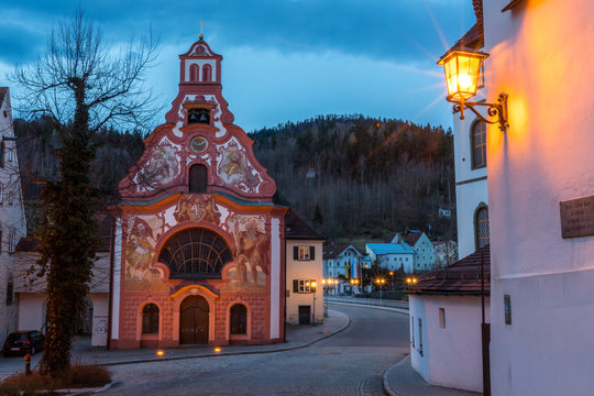 Beleuchtete Heilig-Geist-Spitalkirche in der Altstadt von Füssen am frühen Morgen