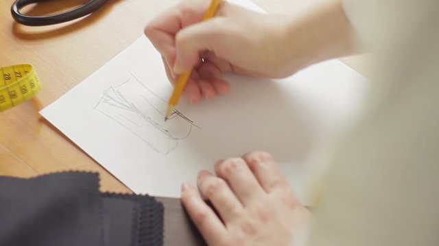 Close-up of a woman's hand, a fashion designer drawing sketches of clothes in the atelier
