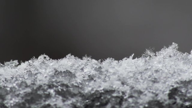 Macro shot of wet snow falling and building up, the crystalline structure of some flakes are evident, as they slowly melt and turn to slush.