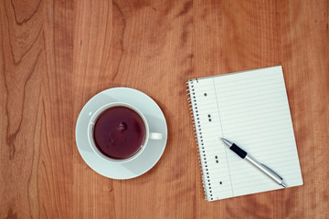 notepad and a cup of tea on wooden table from abov