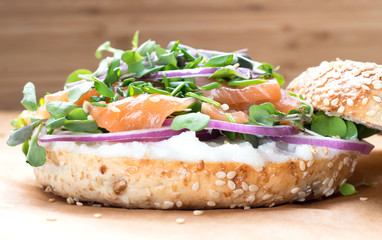 Bagel sandwich with creame cheese, salmon,onion,tomato,greens,chives close-up on a wooden background. Delicious bagel, golden bake color, soft inside, crispy outside.