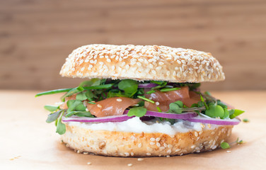 Bagel sandwich with creame cheese, salmon,onion,tomato,greens,chives close-up on a wooden background. Delicious bagel, golden bake color, soft inside, crispy outside.