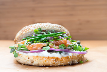 Bagel sandwich with creame cheese, salmon,onion,tomato,greens,chives close-up on a wooden background. Delicious bagel, golden bake color, soft inside, crispy outside.