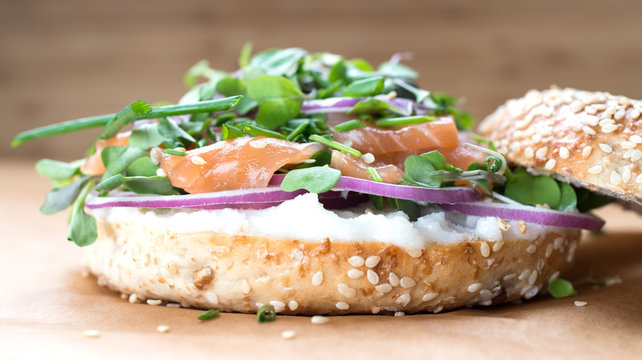 Bagel sandwich with creame cheese, salmon,onion,tomato,greens,chives close-up on a wooden background. Delicious bagel, golden bake color, soft inside, crispy outside.