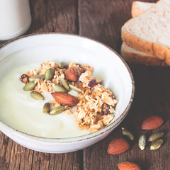 Bowl of homemade granola with yogurt and almond on wooden table