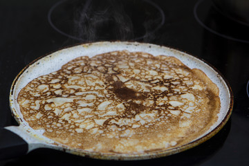 close-up cooking pancakes in a frying pan with a wooden stick