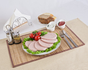 Sliced boiled sausages with tomatoes on lettuce leaves are laid on a plate.