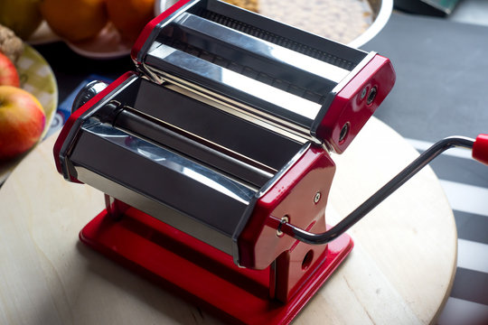 Red iron machine for making homemade pasta or spaghetti standing on the wooden kitchen table. 
