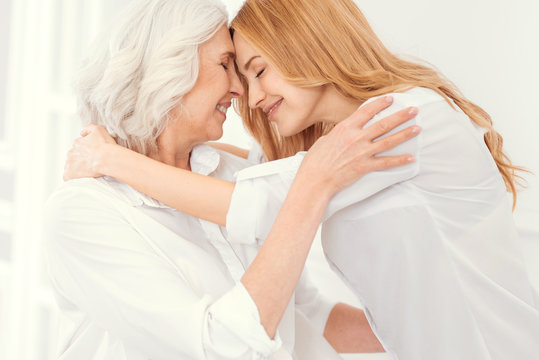 Love you as deep as the ocean. Tender senior mother and her mature daughter smiling and keeping their eyes closed while hugging and expressing their love to each other.