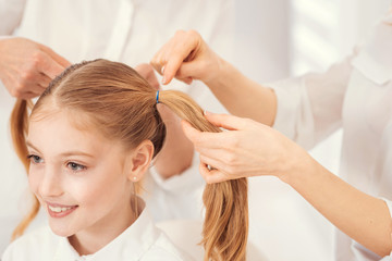 Fototapeta premium Every girls routine. Scaled up look on a cheerful girl sitting on a chair while her loveful mother and grandma standing next to her and doing her hair at home.