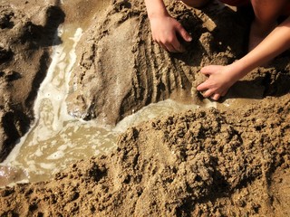 Building a sand castle or a dam in the sand at the beach in summer